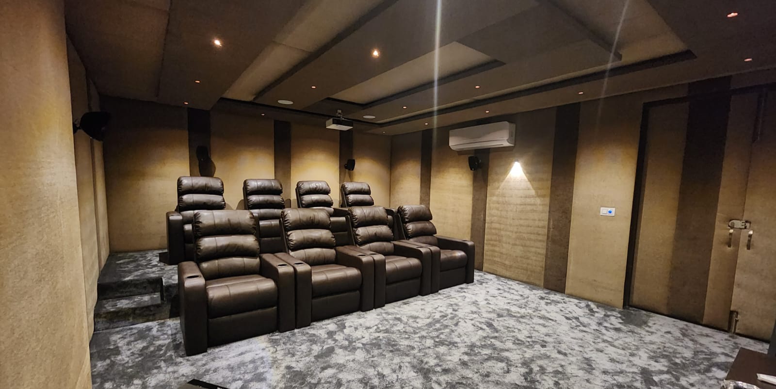 Two tiered rows of tan leather home-theatre recliners with cup holders and a carpeted riser step