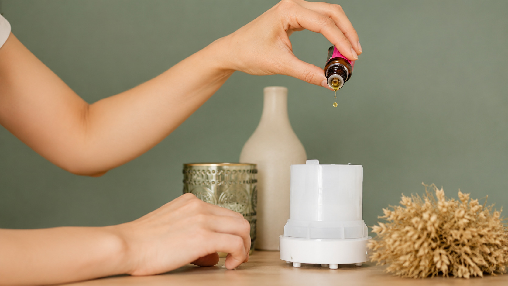Hands adding essential oil to a diffuser in a cozy bedroom for relaxation and improved sleep quality.