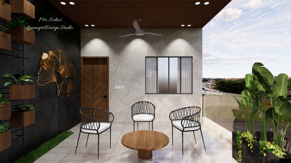 In this image we can see the balcony view,where main accent wall beside the door designed with black marble finish tiles with a brass finish wall mural & plantary boxes at the corner for aesthetic purpse, chairs & centre table is placed at the centre with a combination of pvc ceiling.